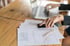 Hände einer Person arbeiten mit Laptop, Smartphone und Diagrammen auf einem Holztisch.