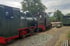 Schwarze Dampflokomotive mit rotem Fahrwerk und der Nummer 2 auf den Schienen neben einem weiteren Zugteil.