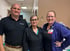 Three healthcare professionals smile in a clinic hallway; one wears a badge identifying her as an LPN.