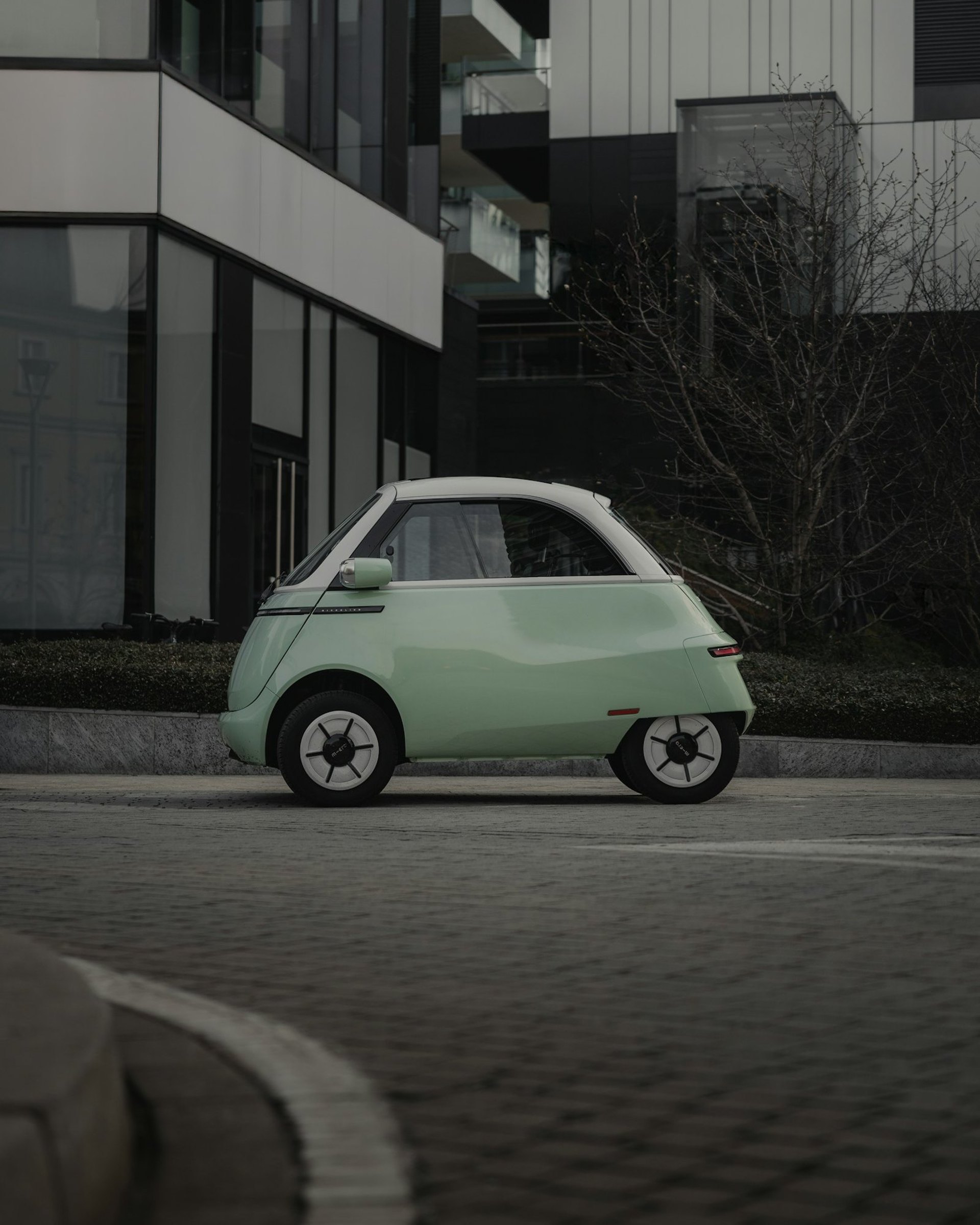 Mintgrüner Microlino vor moderner Architektur