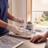 Gloved healthcare professional holds blood sample vials over a medical tray with a centrifuge and knee anatomy on a tablet.
