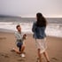 Ein lächelnder Mann macht einer Frau am Strand einen Heiratsantrag und hält ihr kniend ein Ringkästchen entgegen.