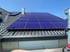 Blaue Solarmodule auf einem dunklen Ziegeldach unter blauem Himmel.
