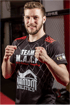 Ein junger Mann im schwarzen T-Shirt mit der Aufschrift „TEAM M.A.A.F. Hi-Ki-Kickboxen-Grappling“, ballt die Fäuste.