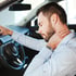 A man in a car, holding his neck in pain after a collision.