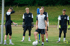 Ein Fußballtrainer steht mit einem Ball vor vier jungen Torhütern auf einem grünen Feld.