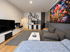 Modernes Wohnzimmer mit grauem Sofa, großem Fernseher, Wandbild mit bunten Pilzen und einem Fahrrad an der Wand.