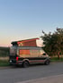 MAN Reisemobil mit geöffnetem Aufstelldach bei Sonnenuntergang auf einer Wiese – hochwertiger Camperausbau für individuelles Vanlife und Campingurlaub in der Natur