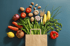 Frisches Gemüse und Obst wie Tomaten, Karotten, Kartoffeln, Bananen und Zwiebeln ragen aus einer Papiertüte.