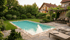 Ein Hinterhof mit einem Pool, Rasen, Blumenbeeten und einer Terrasse mit Gartenmöbeln vor einem Haus bei Sonnenuntergang.