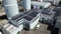 Luftaufnahme eines Industriegeländes mit Solarpaneelen auf einem Flachdach neben hohen Silos und weißen Lieferwagen.