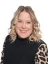 Eine lächelnde Frau mit blonden Locken und einem schwarzen Pullover mit Leopardenärmeln.