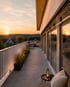 Moderner Dachbalkon mit Loungemöbeln, Pflanzenkübeln und Sonnenuntergang über einer Stadtlandschaft.