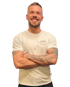 Lächelnder Mann mit Bart, kurzen Haaren, T-Shirt mit "SANNY PERSONAL TRAINER" Aufdruck und tätowierten Armen.