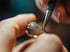 Ein Juwelier bearbeitet einen silbernen Diamantring mit einem präzisen Werkzeug.
