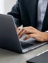 Eine Person in einem Anzug tippt auf einer Laptoptastatur.