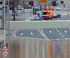 Überschwemmte Straße mit orangefarbenem Transporter und Autos auf der oberen, trockenen Fahrbahn neben einer Schutzwand.
