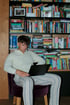 Junger Mann im Hoodie sitzt auf einem Stuhl, benutzt einen Laptop vor einem Bücherregal.