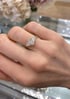 Goldener Verlobungsring mit asymmetrisch angeordneten Diamanten an einer Hand vor hellem Hintergrund.