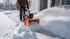 Mann räumt Schnee mit einer orangefarbenen Schneefräse von einem gepflasterten Gehweg vor einem Haus.