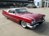 Ein roter Cadillac Oldtimer mit weißem Verdeck, markanten Heckflossen und Weißwandreifen auf einem Parkplatz.