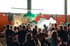 Ein Mann im orangefarbenen Sweatshirt schwebt über einer tanzenden Menschenmenge bei einem "Move In School"-Event.