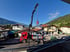 Roter LKW mit Kran hebt Fensterglas über ein Haus in einer Berglandschaft.
