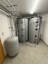 Zwei große graue Wassertanks mit Isolierung und ein kleinerer grauer Druckbehälter in einem Heizungsraum mit Rohren und Beleuchtung Reutte