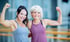 Zwei Frauen lächeln und zeigen ihre Bizeps im Fitnessstudio.