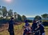 Drei Kinder auf Motocross-Motorrädern und ein Erwachsener schauen auf eine Rennstrecke mit dem Meer im Hintergrund.
