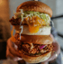 Ein großer Hähnchen-Cheeseburger mit geschmolzenem Käse, Mayonnaise, Salat und roten Zwiebeln, gehalten von Händen.