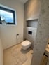 Modernes Badezimmer mit schwebender Toilette, grau gefliesten Wänden, Fenster mit Bergblick und beigem Boden. Reutte