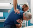 Chiropractor adjusts an older man's painful back in a medical office.
