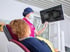 Zahnärztin mit Maske und OP-Haube erklärt einer Patientin eine digitale Röntgenaufnahme des Kiefers am Monitor.