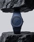 Dunkelblaue Uhr mit achteckigem Gehäuse und Armband, zwischen zwei schwarzen, rauen Steinen platziert.
