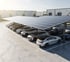 Autos parken unter einem Solardach auf einem Parkplatz vor Industriegebäuden.