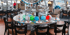 Rundtisch mit Tellern, Hüten und bunten Luftballons, umgeben von dunklen Stühlen in einem Restaurant mit Achterbahn.