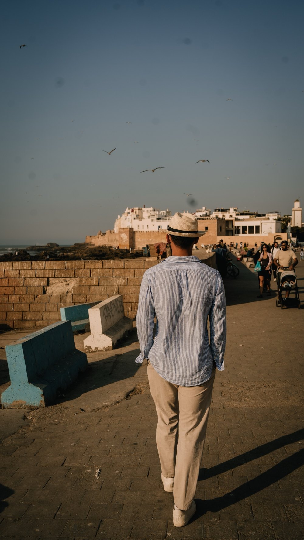 Mann mit Strohhut geht auf der Hafenmauer auf die Altstadt von Essaouira zu