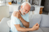 Senior man with shoulder pain, possible arthritis discomfort sitting on sofa