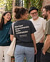 Gruppe im Gespräch, im Vordergrund ein anthrazitfarbenes Wearmorrow® Shirt mit der Rückenbotschaft Weniger gegeneinander Mehr miteinander