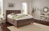 Braunes Boxspringbett mit gepolstertem Kopfteil in einem hellen Schlafzimmer mit beigem Teppich.