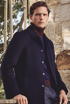 Mann in dunkelblauer Jacke und Rollkragenpullover vor Natursteinwand – klassischer Herbstlook mit urbanem Charme.

