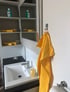 Gelbes Handtuch hängt an einem Haken neben einem Waschbecken mit Seifenspender.