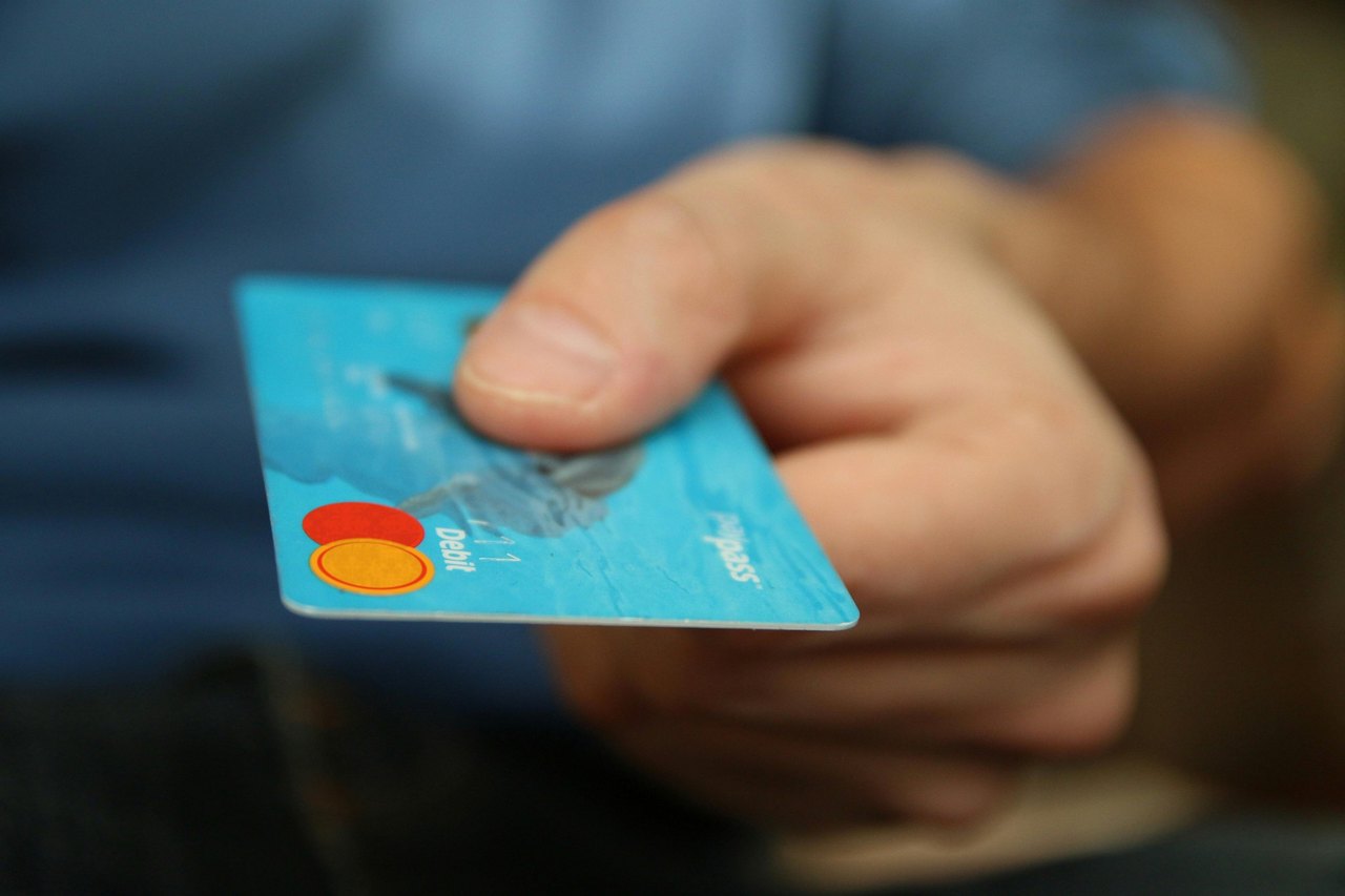 Eine Hand hält eine blaue Debitkarte mit Mastercard-Logo und dem Schriftzug Paypass nach vorne.