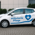 Weißes Auto mit der blauen Aufschrift „ambulante Pflege“ und einem Herz-Symbol mit weißem Kreuz auf der Beifahrerseite.