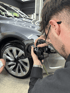 Mann mit Kamera fotografiert graues Auto, Nahaufnahme von Rad und Reifen. Mikael Pyrek beim Kunden von Codeme