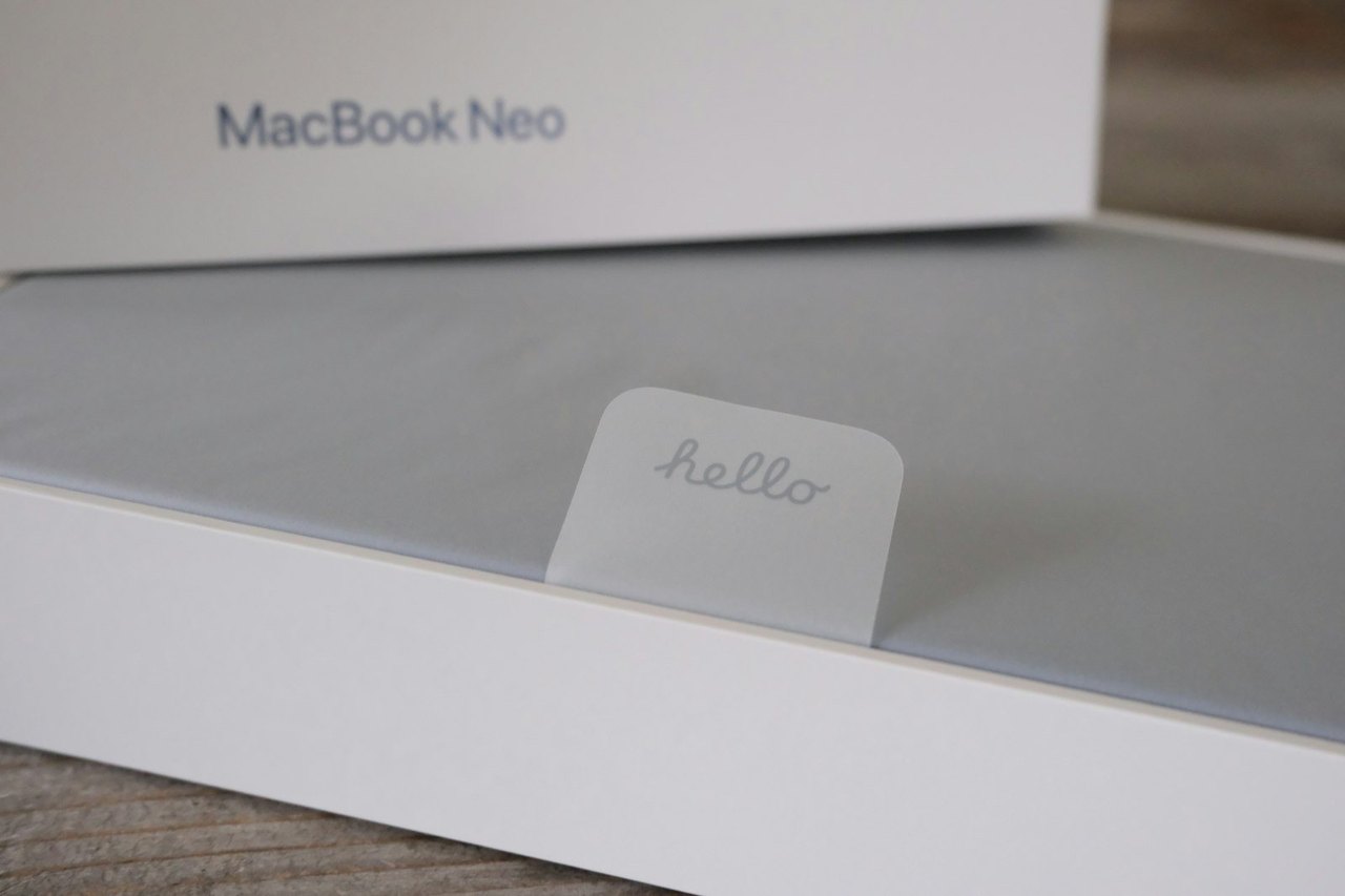 Geöffneter MacBook-Karton, darin das Gerät mit einem Aufkleber mit dem Wort hello
