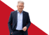 Mann mit Brille und Anzug steht vor rot-grünem Hintergrund.