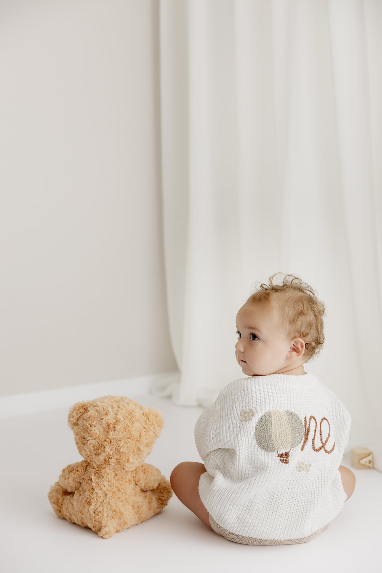 Kleinkind sitzt mit dem Rücken zur Kamera neben einem Teddybären