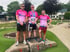 Drei Läufer in pinken Diakonie-Laufshirts auf einem Siegerpodest.